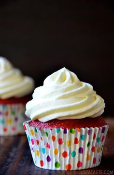 two cupcakes with white frosting and colorful polka dot paper wrappers on a table