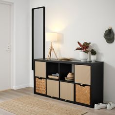 a black and beige cabinet with baskets on it next to a white wall in a living room