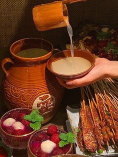 a person pouring liquid over skewers of food