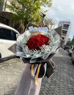 a woman holding a bouquet of red and white flowers in her hand on the street