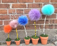 four potted plants with fake pom - poms in front of a brick wall