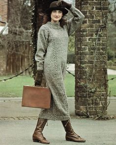 a woman in a gray sweater dress and brown boots is holding a suitcase while standing on the sidewalk