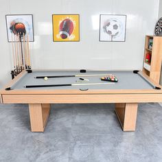 a pool table with cues and balls on it in front of two pictures hanging on the wall