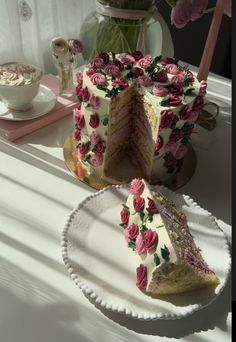 a white cake with pink flowers on it sitting on a table next to a vase