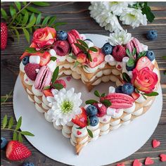 a heart shaped cake decorated with flowers and berries on a plate next to strawberries