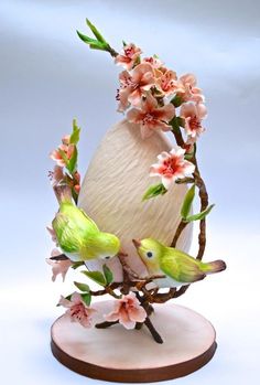 two green birds are perched on a branch with pink flowers and branches in the shape of an egg