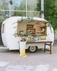 an old camper converted into a food truck with flowers and greenery on the back