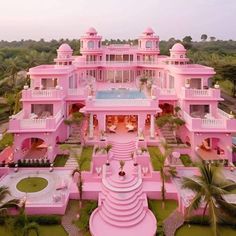 an aerial view of a pink mansion with pool in the foreground and palm trees surrounding it