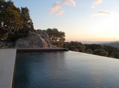 an empty swimming pool in front of a large rock formation at sunset or dawn with the sun setting on the horizon