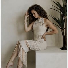 a woman sitting on top of a white table next to a plant