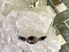 This 1.8 mm Sterling Silver Petoskey stone bracelet features a lovely Oval Petoskey stone surrounded by Leland blue chip beads and sterling silver beads. The bracelet chain is fully adjustable to a maximum of 8.5 inches using a move able coin-shaped silicone lined bead that slides along the chain. This chain is plated with fine silver to ensure a bright white color and protect against tarnish. Petoskey stones aren't real stone but rather a fossilized coral only found in the northern portions of Adjustable Oval Bracelets As Gift, Adjustable Oval Bracelet For Gift, Adjustable Oval Bracelets, Adjustable Oval Bracelets For Everyday, Adjustable Sterling Silver Gemstone Bracelet Gift, Adjustable Sterling Silver Beaded Bracelets With Stones, Adjustable Sterling Silver Bracelet With Natural Stones For Gift, Adjustable Oval Bracelet With Natural Stones, Adjustable Oval Spiritual Bracelets