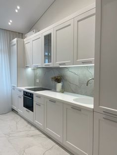 a kitchen with white cabinets and marble counter tops, along with a window in the background