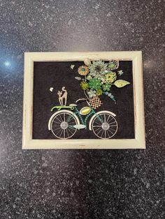 an embroidered bicycle with flowers on the front and back wheel is displayed in a frame