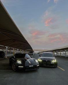 two black cars parked next to each other on a parking lot at dusk with the sky in the background