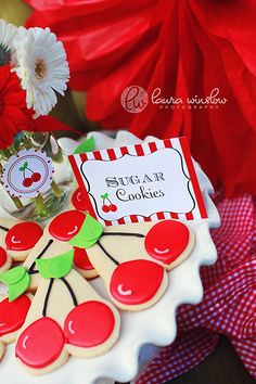 a decorated cake with cherries and cookies on it sitting on a table next to flowers