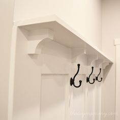 a white shelf with hooks on it in a room that is painted white and has two black hooks attached to the wall