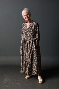 an older woman standing in front of a gray background wearing a dress with floral print