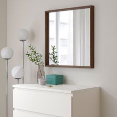 a white dresser topped with a mirror next to a vase filled with green plantes