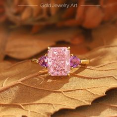 a pink diamond ring sitting on top of a leaf covered ground with the words gold jewelry art written below it