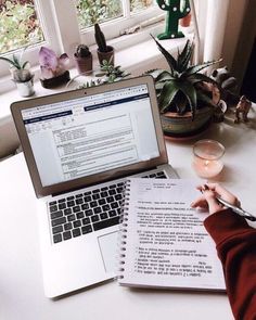 a person sitting in front of a laptop computer on top of a white desk next to a plant