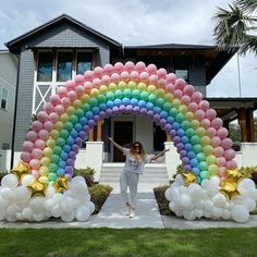 a woman standing in front of a large rainbow arch with balloons on the top and bottom