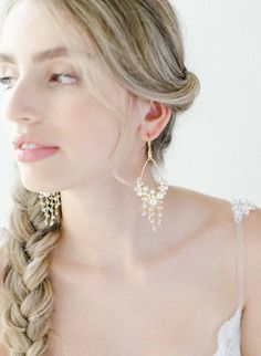 a woman with braids and earrings on her head looking off to the side, wearing a white dress