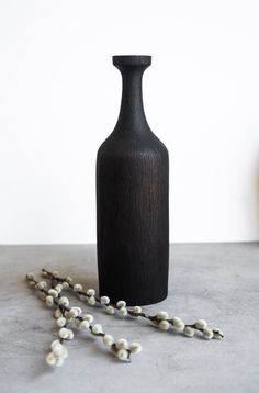 a black vase sitting on top of a table next to a white flower arrangement and a string of beads