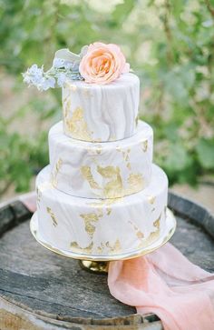 a white and gold wedding cake on top of a wooden barrel