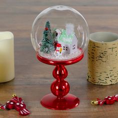 a snow globe sitting on top of a wooden table next to candles and other decorations