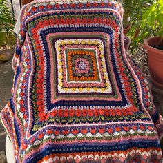 a crocheted blanket sitting on top of a wooden bench next to a potted plant