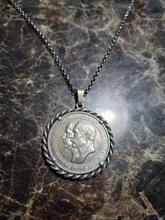 a silver coin on a chain sitting on top of a marble countertop with the image of a man's head