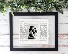 an image of two women hugging each other in a black frame on a white wooden wall