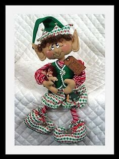 an elf doll holding a teddy bear on top of a white bedding sheet with red and green checkered pants