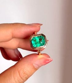 a woman's hand holding a ring with a green stone in the middle,