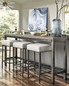 a dining room table with four stools and a painting on the wall