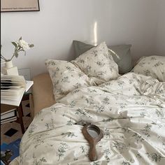 an unmade bed with white sheets and flowers on the comforter, next to a wooden spoon