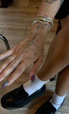 a woman's hands with tattoos and rings on her left hand, sitting next to a chair