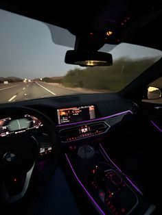 the interior of a car driving down a highway at night with purple lights on it