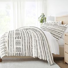 a white bed with black and white patterned comforter in a bedroom next to a window