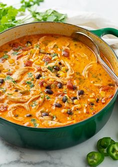 a green pot filled with chicken and bean soup next to some cilantro peppers