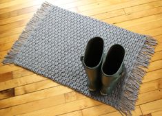 pair of green rain boots sitting on top of a wooden floor next to a gray rug