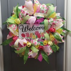 a welcome sign hanging on the front door with flowers and ribbons around it's edges