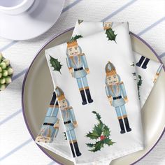 two napkins with nutcracker on them sitting on a plate next to a cup and saucer