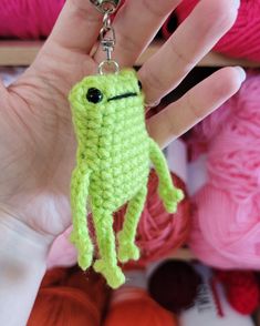 a hand holding a crocheted keychain with a small green creature on it