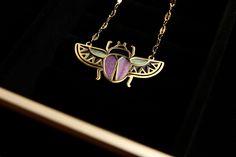 a gold necklace with a purple and green bee on it's back end, sitting on a black velvet surface