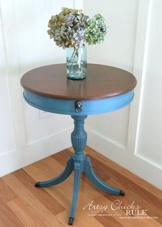 a blue table with flowers in a vase on it's top and wood floors