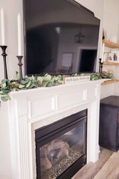 a flat screen tv mounted above a fireplace with candles and greenery on the mantle