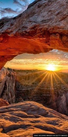 the sun is shining through an arch in the rock formation, with red rocks surrounding it