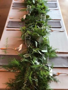 a long table with place settings and greenery on it