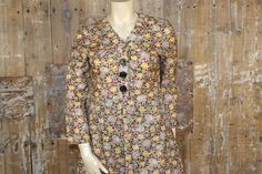 "Vintage floral tea dress, made by Gigi in 1970s. Made from a lightweight polyester fabric, it has a design of yellow, green and beige roses on a black background. It has a fitted bodice with a V-neckline, bracelet length sleeves, and buttons down to the waist. The skirt is flared and just below knee length. Fastens with a zip at the back. Labelled size 44, in my opinion would fit a current UK 14/ 16. Please check measurements carefully. Measures 42\" bust, 34\" waist, 45\" hips. Length 16\" fro Vintage Long Sleeve Floral Summer Dress, Vintage Floral Long Sleeve Summer Dress, Fitted A-line Vintage Dress With Floral Print, Fitted Green Vintage Dress With Floral Print, Fitted Green Floral Vintage Dress, 1970s Fitted Floral Print Dresses, Vintage Long Sleeve Floral Dress, Retro Vintage Dress With Floral Print For Fall, Fitted Retro Vintage Dress With Floral Print